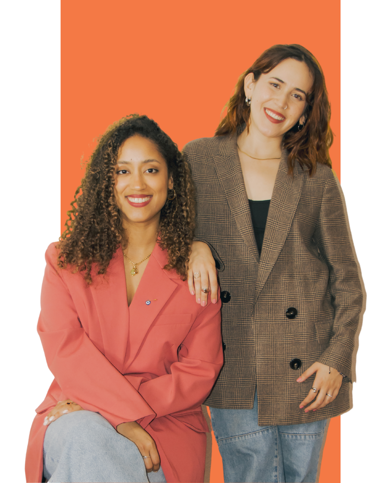Dos mujeres sonriendo, una con cabello rizado en blazer rosa, la otra con cabello ondulado en blazer marrón a cuadros, contra fondo naranja